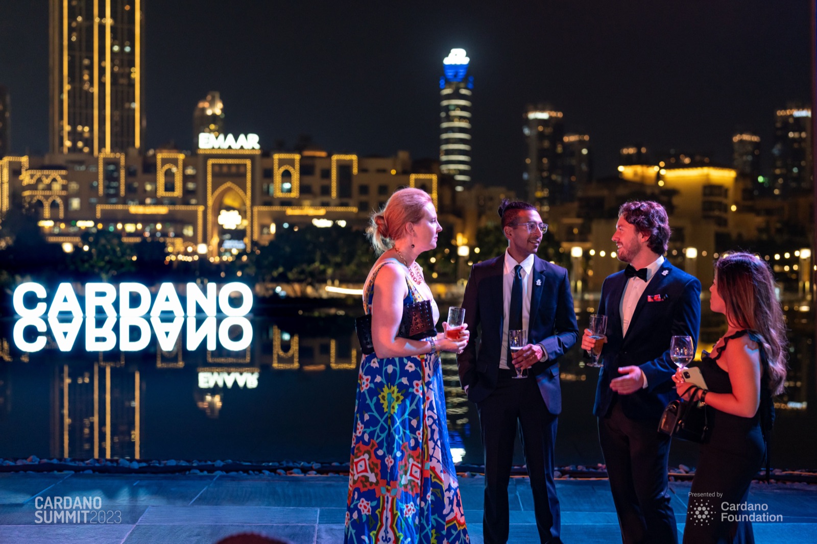 Guests talking at night beside illuminated CARDANO letters, with the Dubai skyline behind